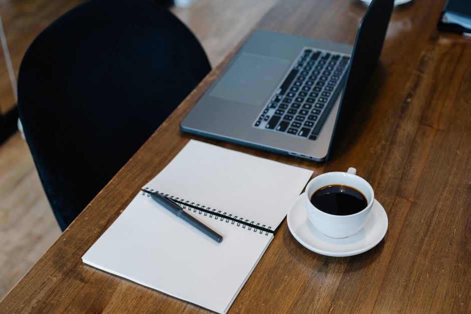 High angle of opened laptop and spiral notebook with blank pages placed on wooden table.