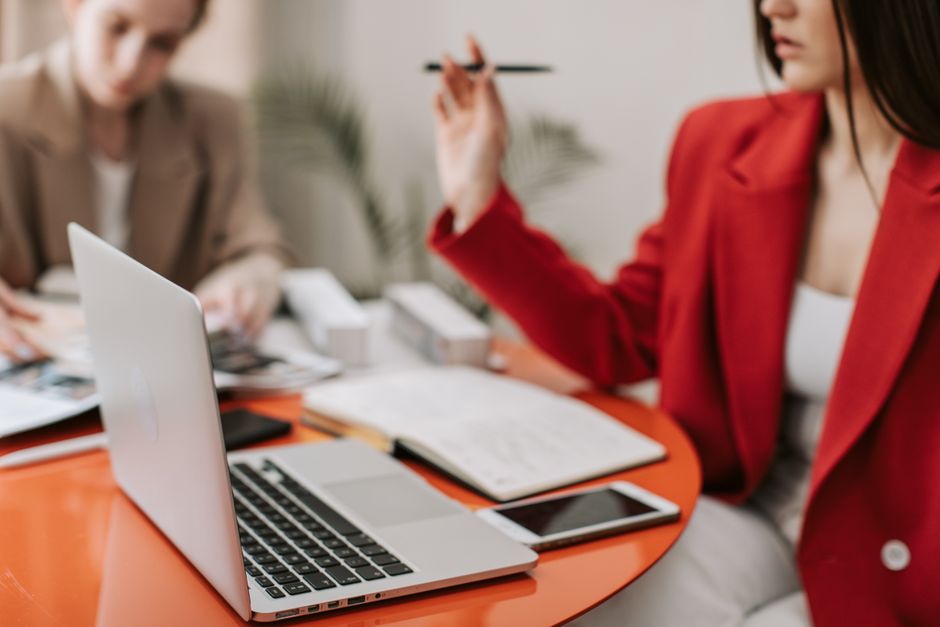 Two professional women working at a desk with a laptop and documents, focused on collaboration.