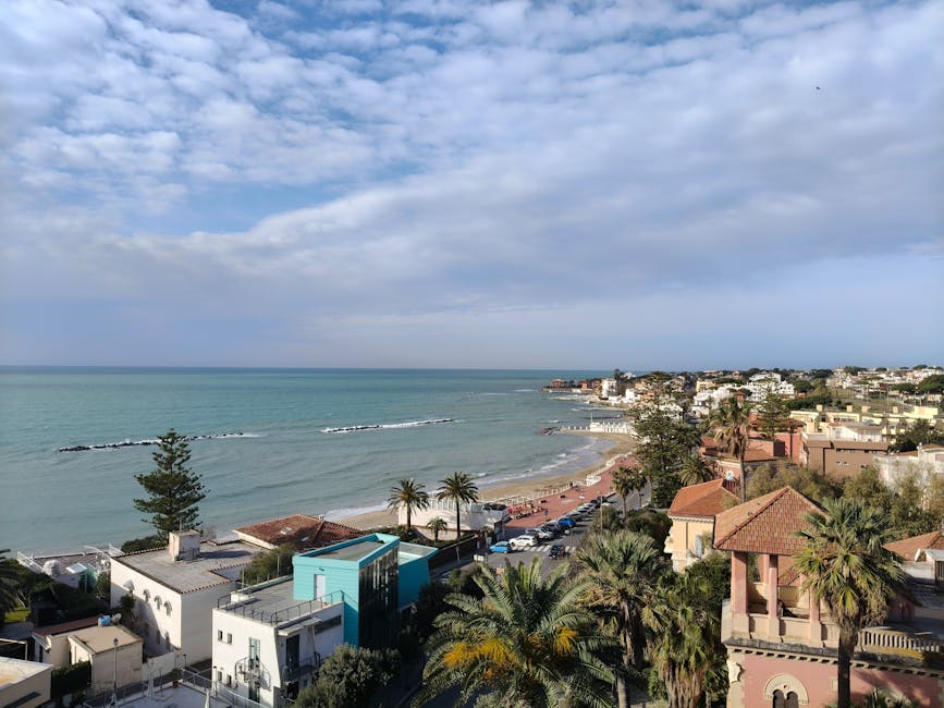 Beautiful coastal town view with beach, sea, and palm trees, under a bright sky